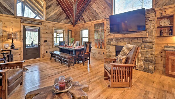 L’intérieur d’un chalet avec un plafond en bois, une cheminée en pierre et un grand téléviseur fixé au mur.