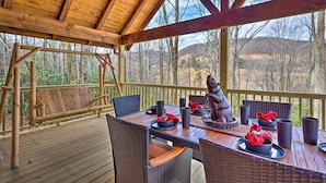Une terrasse en bois avec des meubles en osier, une table dressée pour le repas et une statue d’ours.
