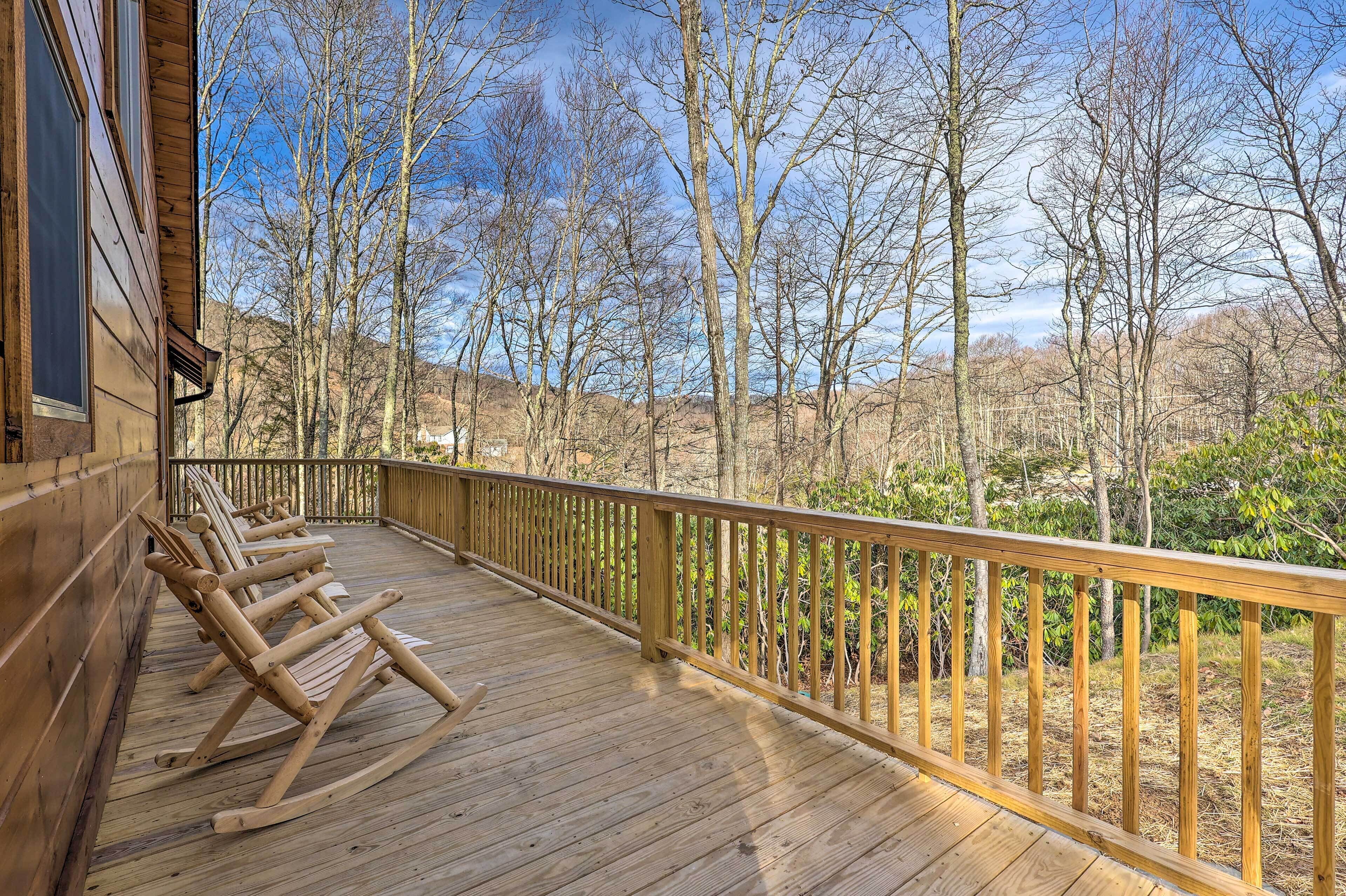 Un terrazzo in legno con poltrone a dondolo, una ringhiera di legno e vista su alberi spogli e colline.