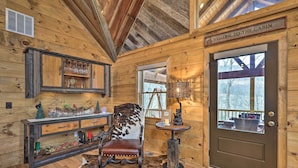 L'intérieur d'une cabane, avec un revêtement mural en bois, un fauteuil en cuir, une console sur laquelle sont disposés des objets en verre et une porte portant l'inscription « Bienvenue dans la cabane ».