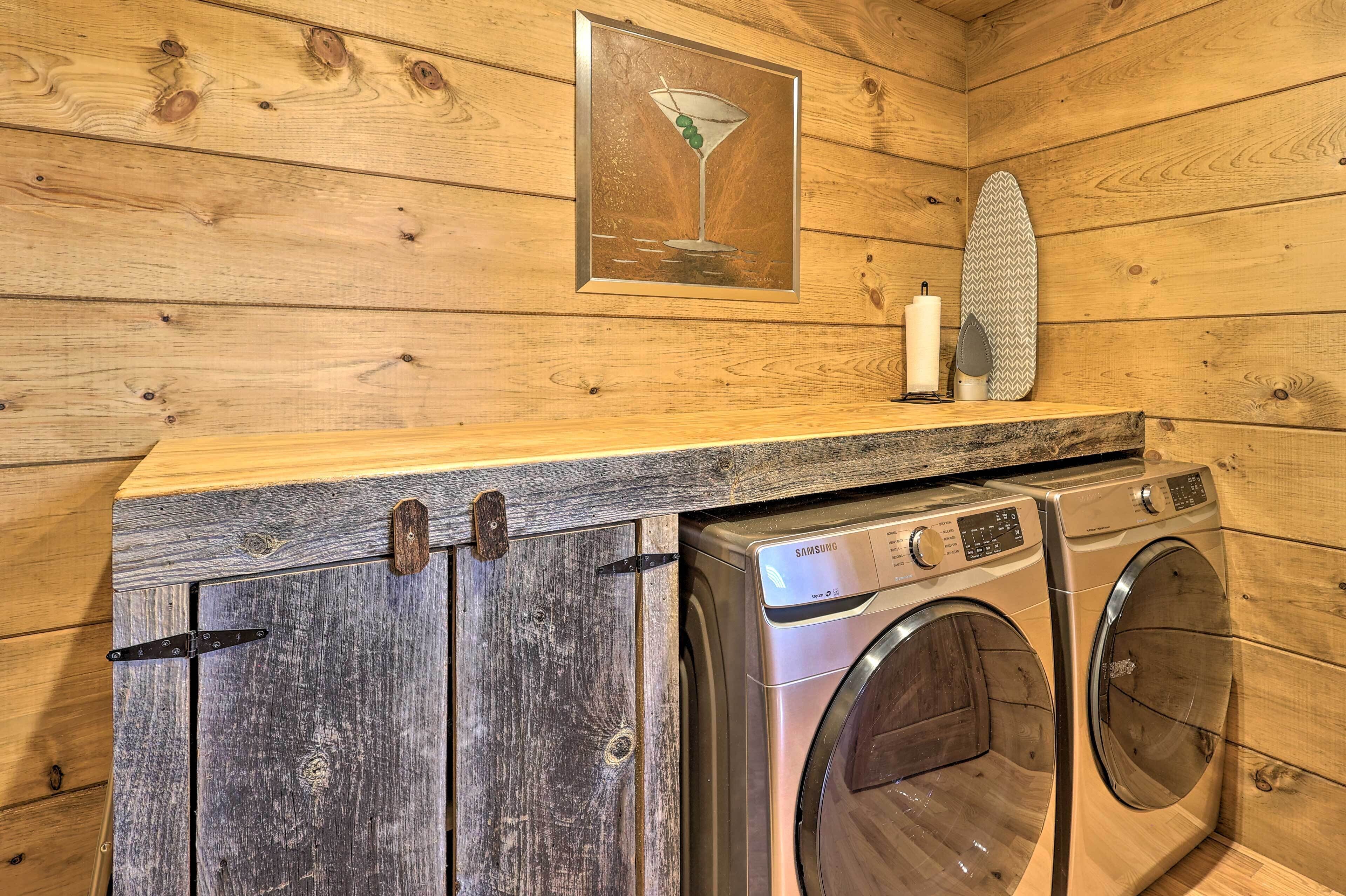 L’intérieur d’une cabane en bois, avec un lave-linge et un sèche-linge, une étagère en bois sur laquelle est posée une photo, et une bougie.
