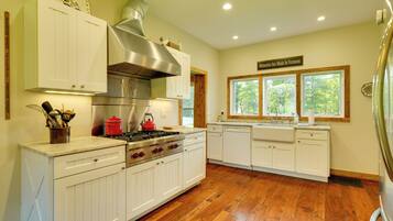 A kitchen with white cabinetry, a stainless steel range hood, a red kettle, and a window with a view of trees.