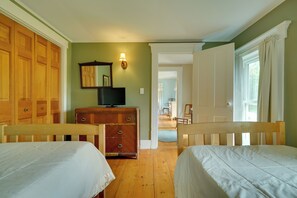 Quarto com duas camas de madeira, cômoda, televisão e janela com cortinas.