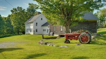 A two-story house with a stone foundation, a large tree in front, and a red tractor parked on the grass.