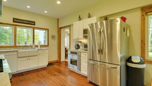 A kitchen with white cabinets, stainless steel appliances, a wooden floor, and a window with a view of trees.