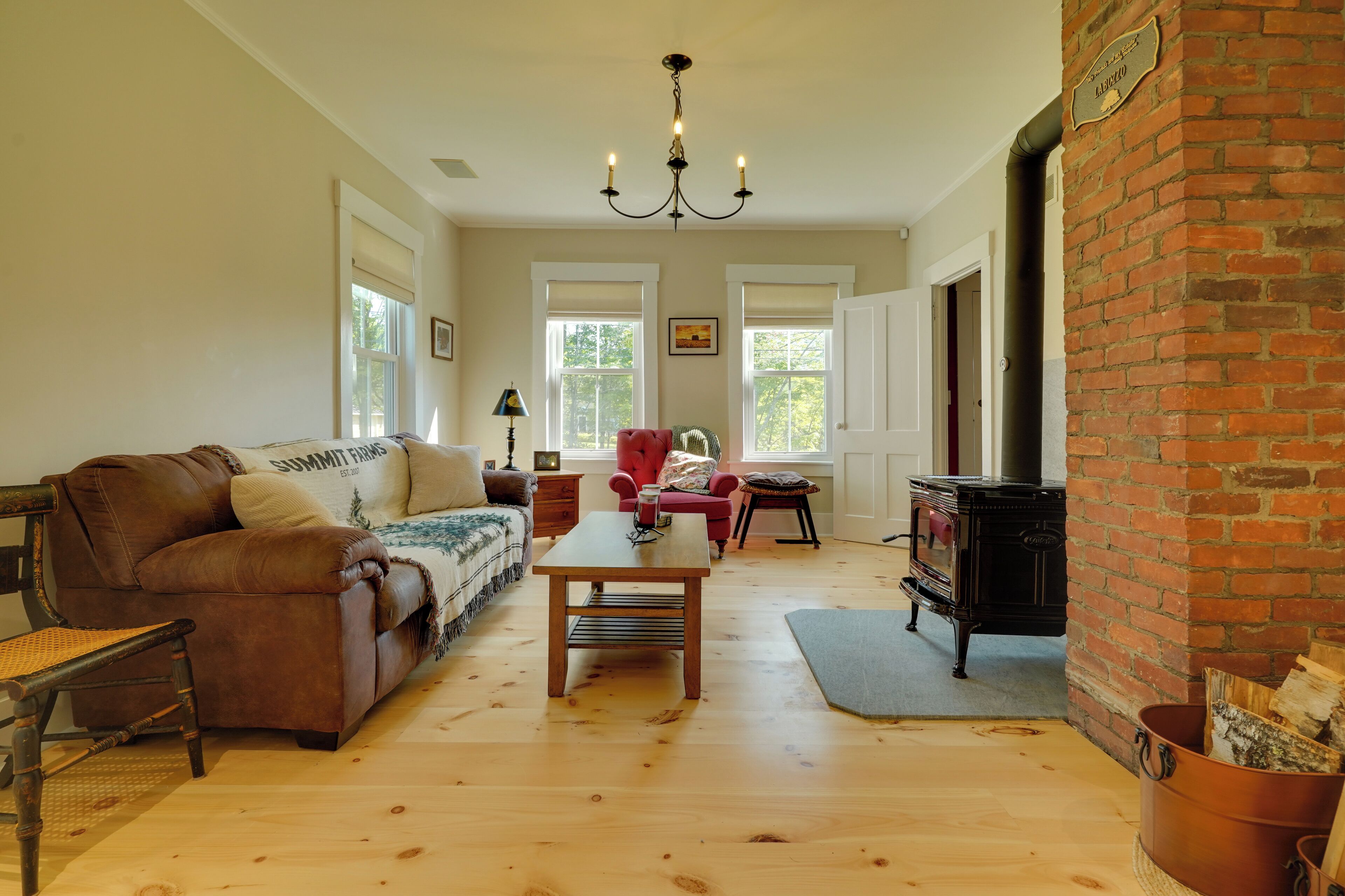 A cozy living room with a leather sofa, a wooden coffee table, a red armchair, and a black wood-burning stove.