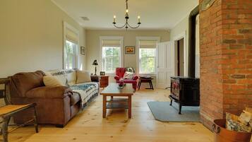 A cozy living room with a leather sofa, a wooden coffee table, a red armchair, and a black wood-burning stove.