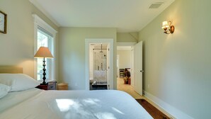 A bedroom with a large bed, a nightstand, a lamp, and a view of a bathroom with a shower.