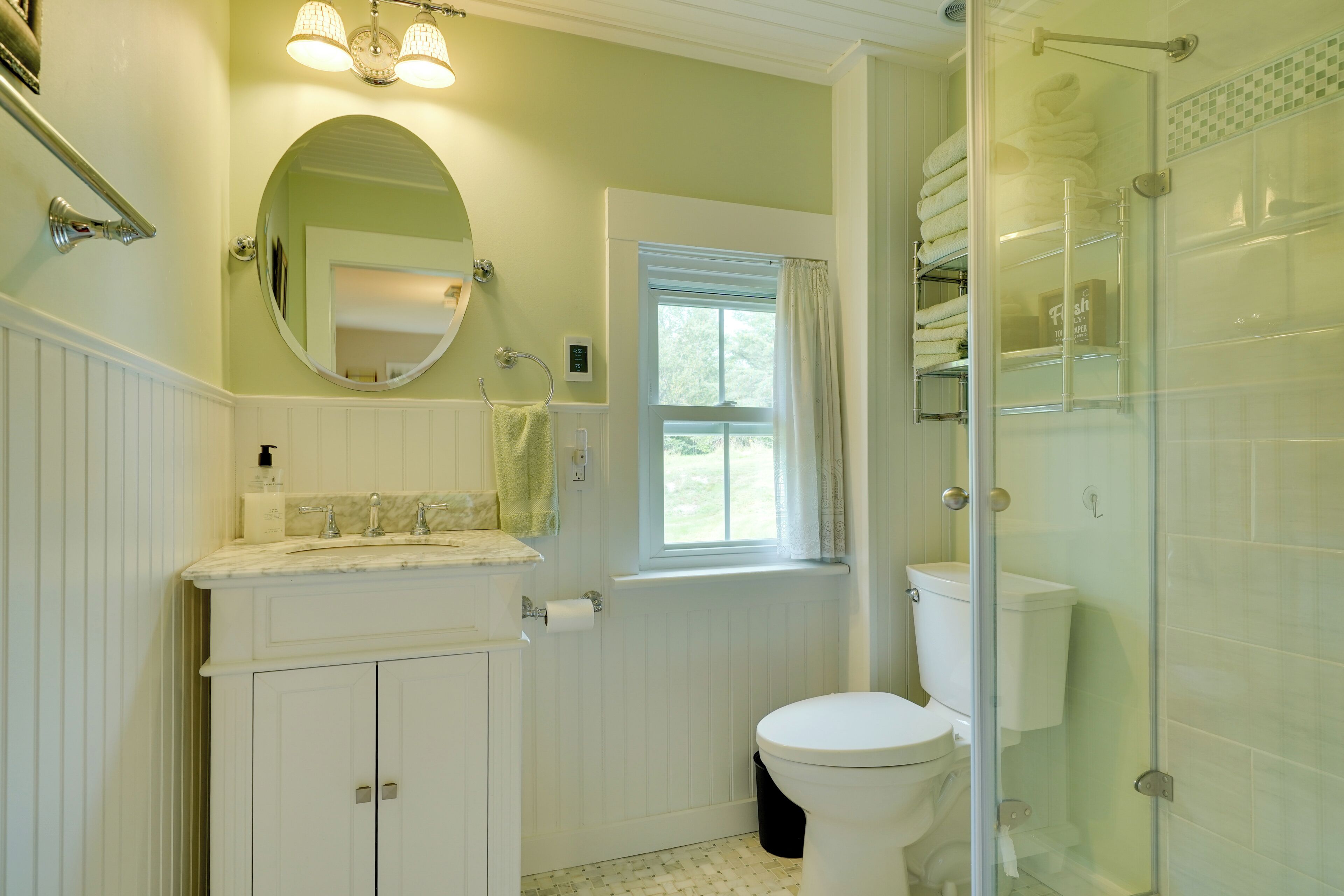 A bathroom with a toilet, sink, mirror, and a glass shower enclosure.