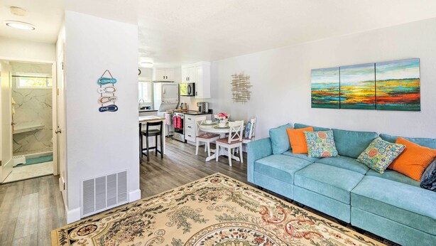 A living room with a blue sofa, a patterned rug, and a painting of a sunset. - Cozy Monterey Apartment - Walk to Wharf & Dtwn! (Monterey)
