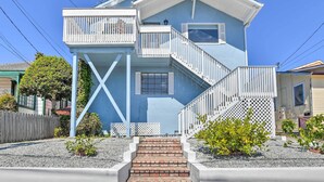 A two-story house with a blue exterior, a white balcony, and a brick staircase leading to the entrance. - Cozy Monterey Apartment - Walk to Wharf & Dtwn! (Monterey)