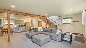 A spacious living area with a grey sectional sofa, ottoman, and a small table. A wooden staircase leads to an upper level. - Upscale Bend Barn w/ Deck - Close to Trails! (Bend)