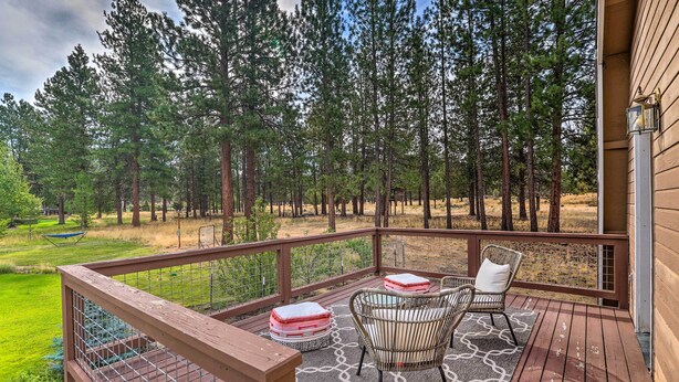 A wooden deck with a view of a forest, a wicker chair, a bench, and a small table with a cushion. - Upscale Bend Barn w/ Deck - Close to Trails! (Bend)