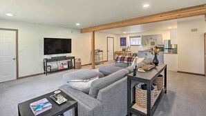 A living room with a grey sofa, a coffee table, a TV, and a kitchen area in the background. - Upscale Bend Barn w/ Deck - Close to Trails! (Bend)