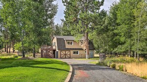 A two-story house with a garage, surrounded by trees and a gravel driveway. - Upscale Bend Barn w/ Deck - Close to Trails! (Bend)