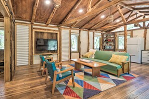 A spacious living area with a wooden ceiling, a green sofa, a coffee table, and a TV. - Unique Stay: Historic Home Along Blanco River (Blanco)