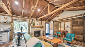 Un intérieur rustique avec une cheminée en pierre, des poutres en bois et un coin repas où une table est dressée pour deux personnes.