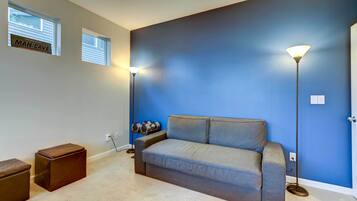 A room with a grey sofa, two small windows, a blue accent wall, and a floor lamp.