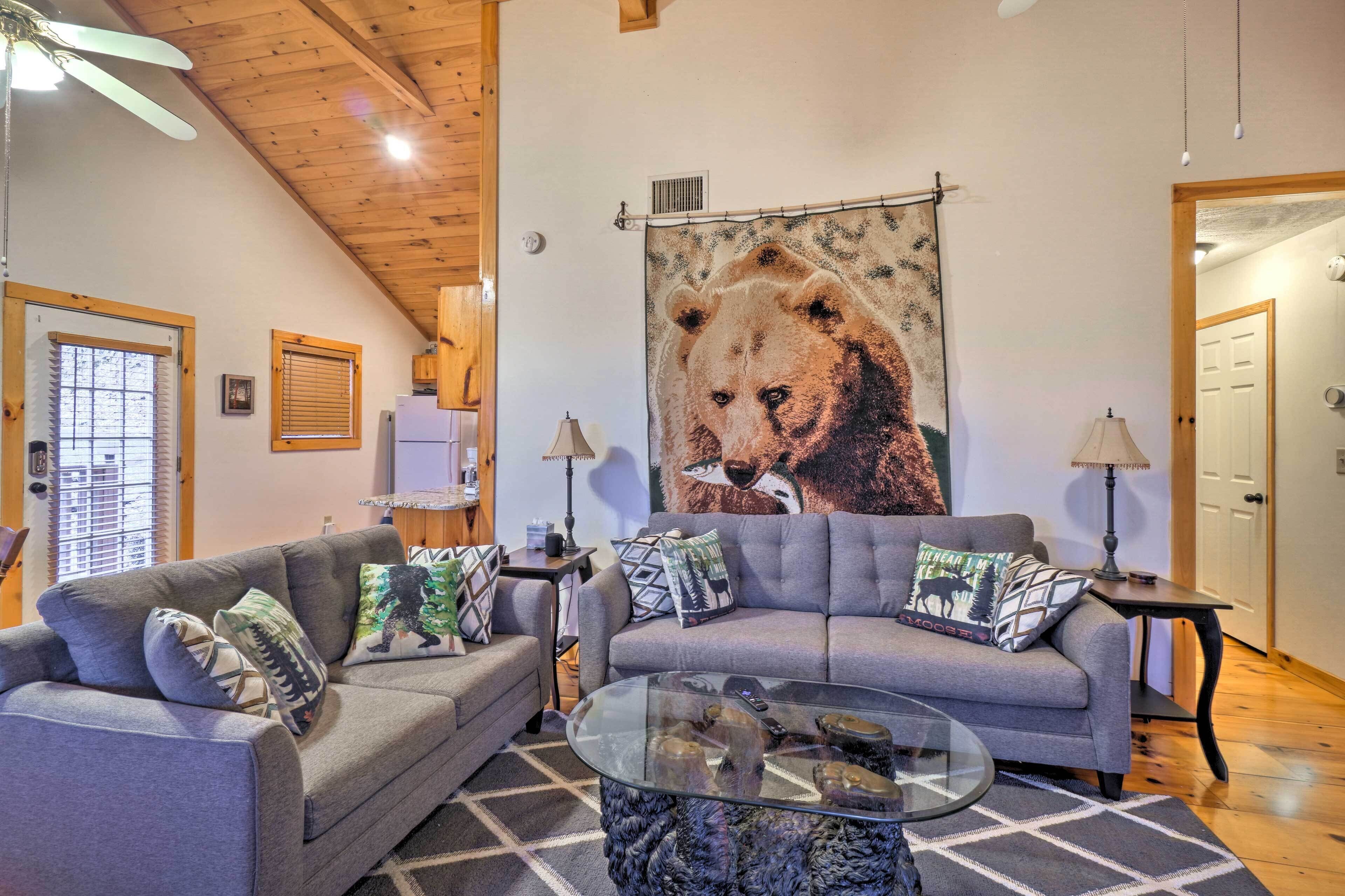 A living room with two grey sofas, a glass coffee table, and a large bear mural on the wall.