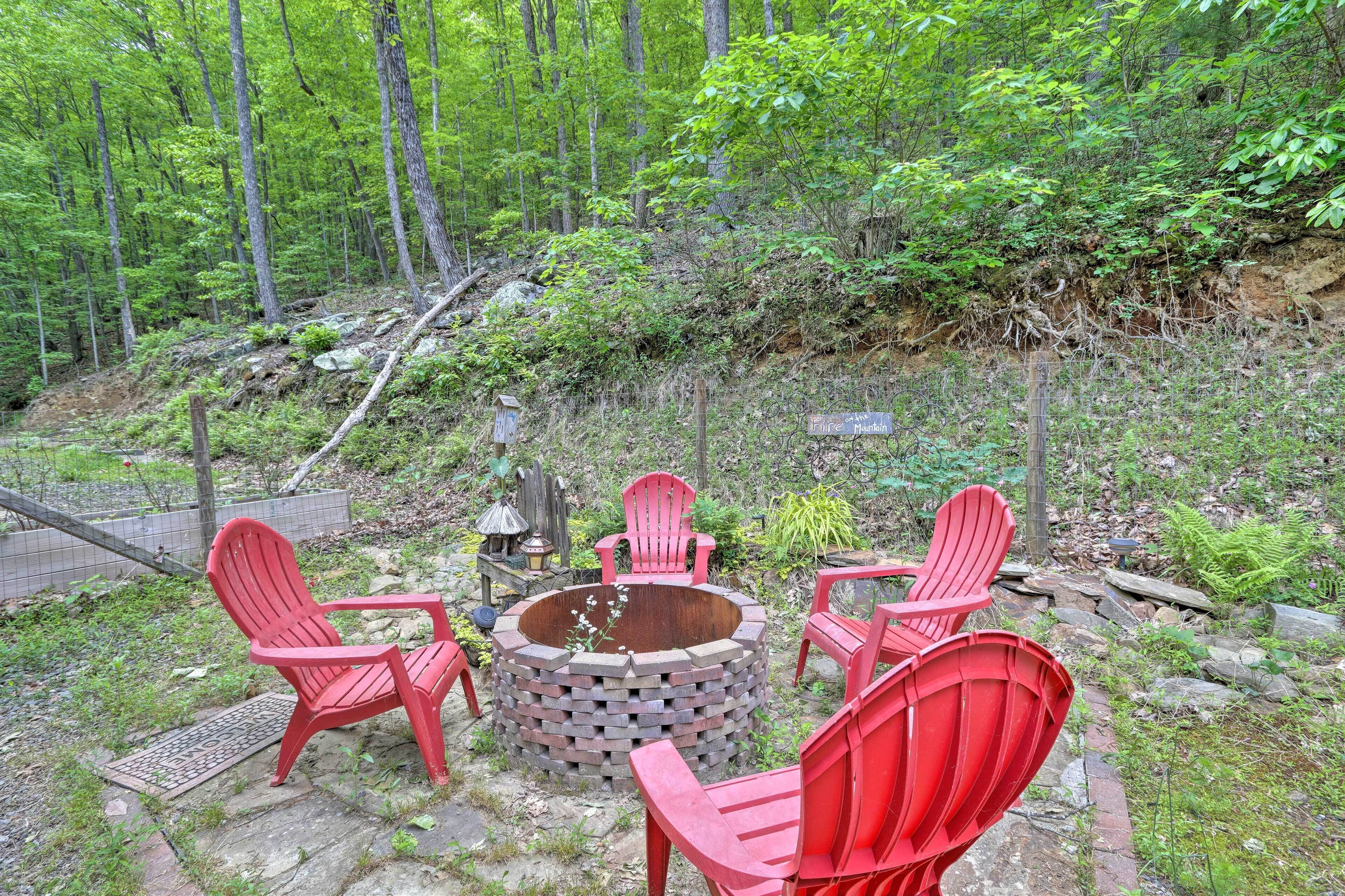 Un foyer circulaire, entouré de quatre chaises Adirondack rouges, se trouve dans une zone boisée.