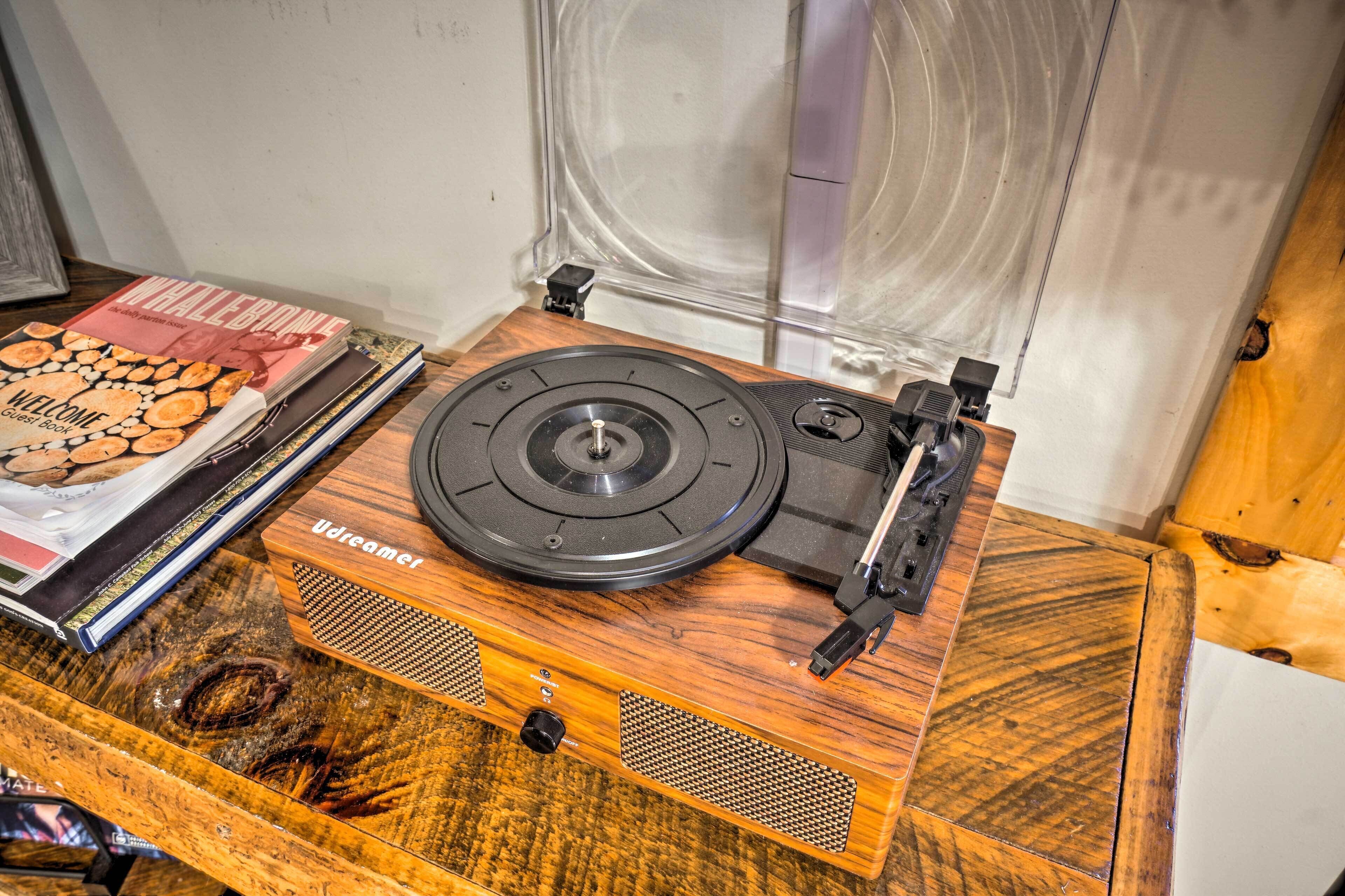 A wooden turntable with a record on it, placed on a table with magazines and a book nearby.