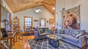 A cozy living room with a wooden ceiling, a gray sofa, a glass coffee table, and a large bear mural on the wall. - Murphy Family Cabin w/ Fire Pit & Forest Views! (Murphy)
