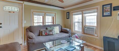 A cozy living room with a brown sofa, a glass coffee table, and a ceiling fan.