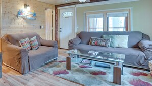 A cozy living room with a wooden ceiling, a glass coffee table, two sofas with patterned cushions, and a decorative wall hanging. - Cozy Houghton Lake Vacation Rental w/ Fireplace! (Houghton Lake)