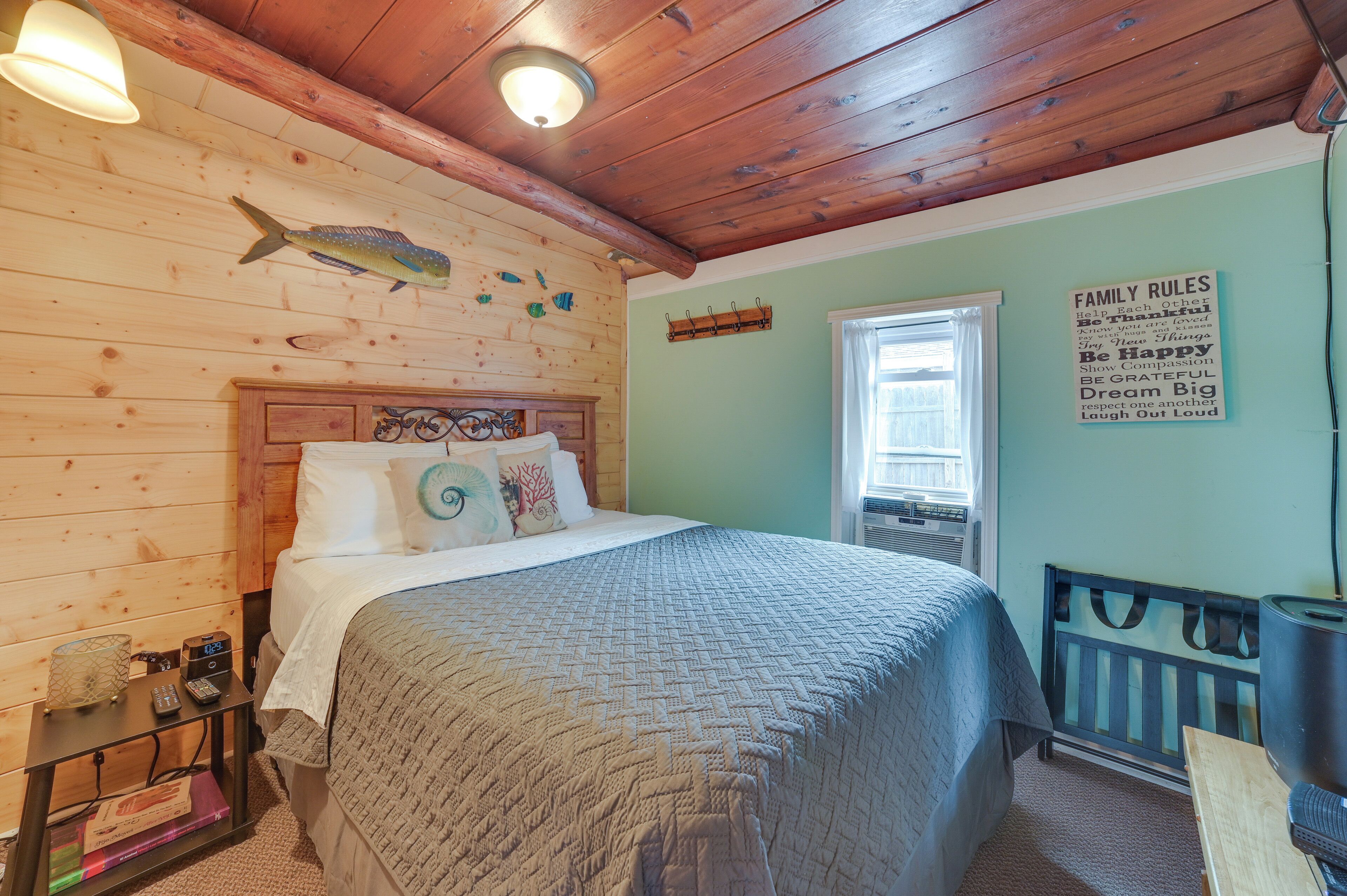 A cozy bedroom with a wooden ceiling, a bed with a quilt, a wall-mounted fish decoration, and a 'Family Rules' sign.