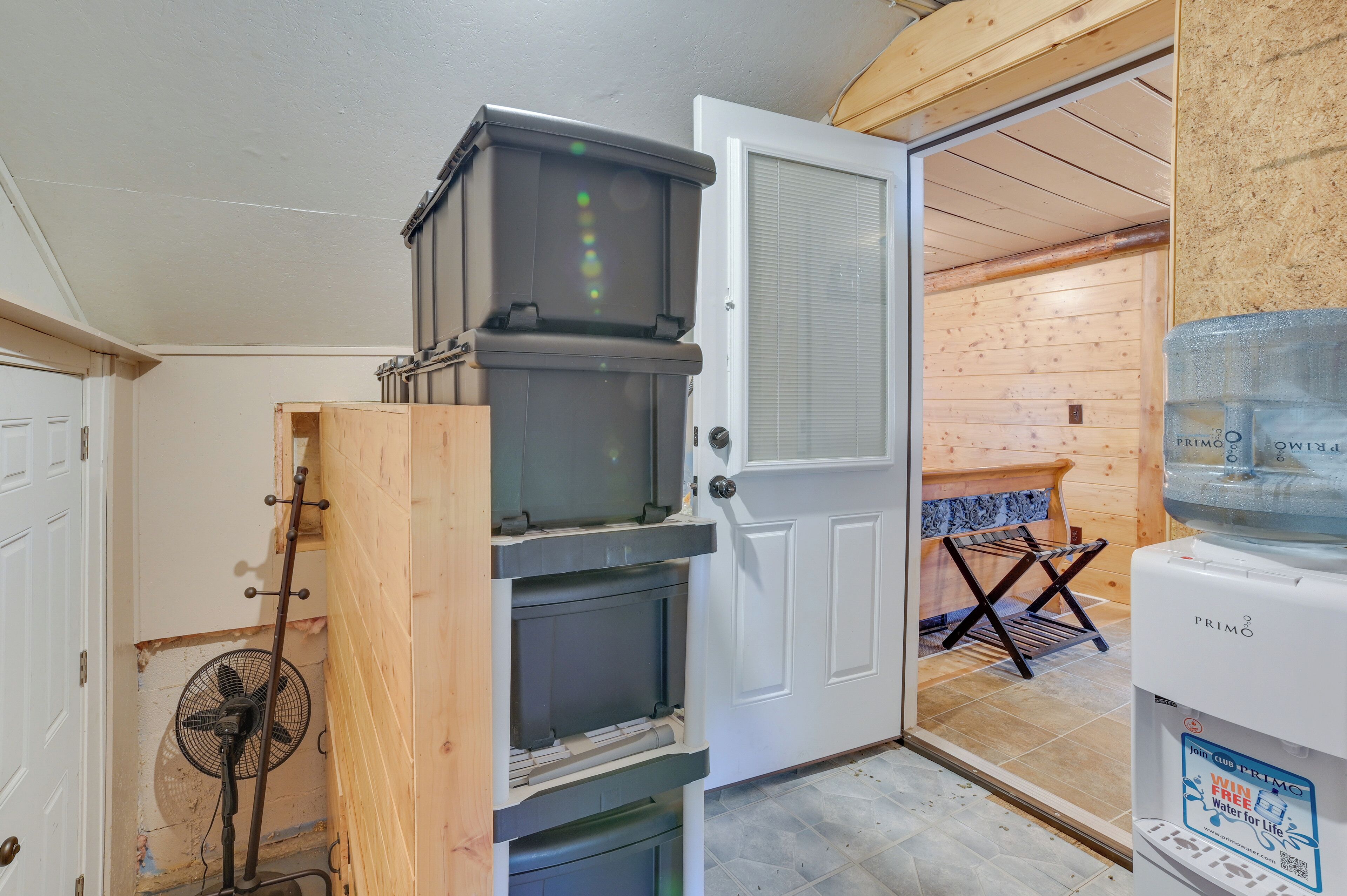 A room with a wooden door, a water dispenser, a fan, and a small table with a towel rack.