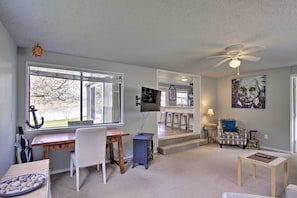 A living room with a wooden desk, a blue heater, a TV mounted on the wall, and a ceiling fan.