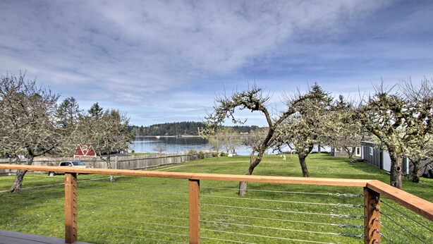 A deck with a wooden railing overlooking a grassy area with trees and a lake. - Waterfront Anderson Island Home w/ Kayaks (Anderson Island)