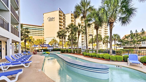 Zwembadgedeelte van een hotel met blauwe ligbedden, helder water en palmbomen.