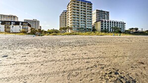 Een hotel aan het strand met meerdere hoge gebouwen, een zandstrand en palmbomen.