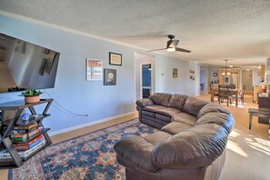 A living room with a brown leather sofa, a patterned rug, a TV on a stand, and a ceiling fan.