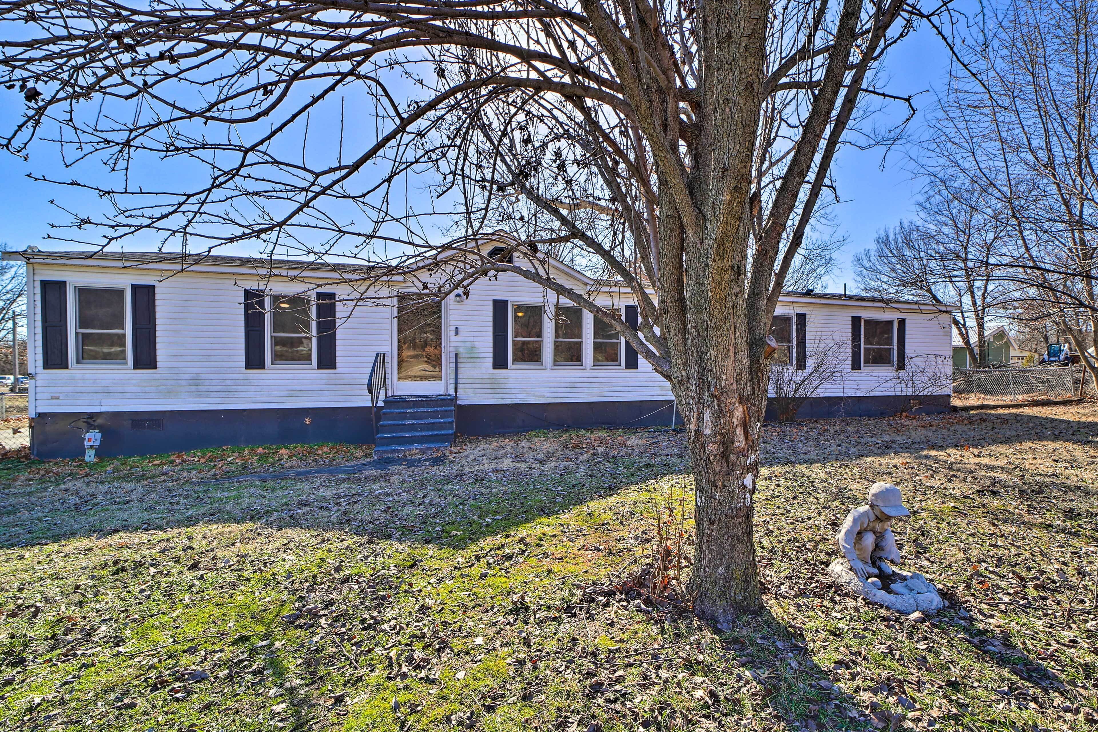 A single-story mobile home with a front porch and a tree in front.