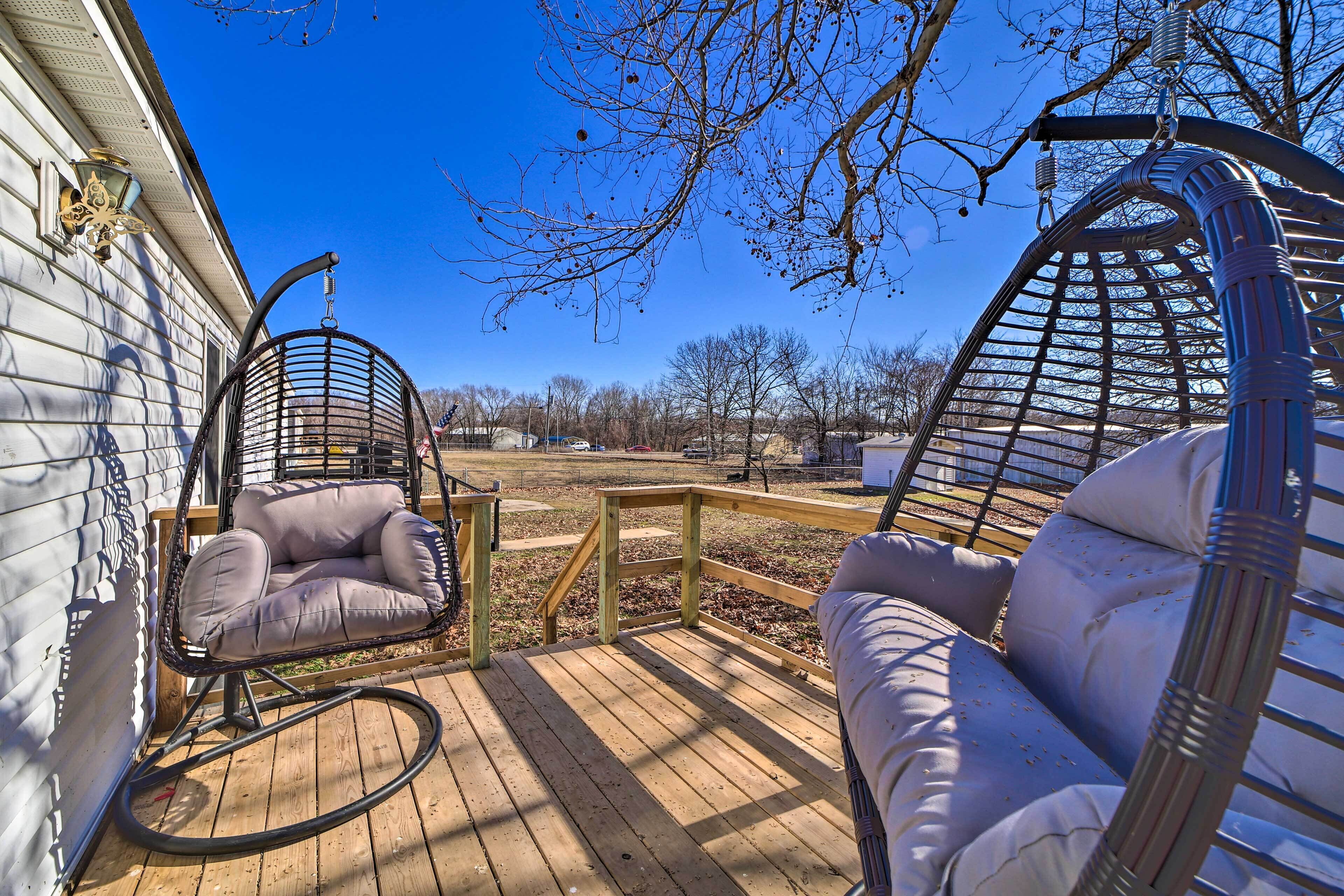 A wooden deck with two wicker swing chairs and a cushioned bench.