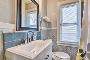 A bathroom with a white sink, a toilet, a mirror, and a window with blinds. - Detroit Apartment - 5 Mi to Downtown! (Detroit)