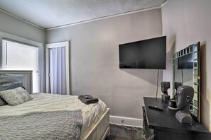 A bedroom with a bed, a flat-screen TV, a dresser with a bust sculpture, and a window with blinds. - Detroit Apartment - 5 Mi to Downtown! (Detroit)