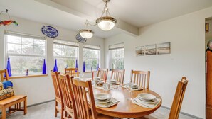 A dining room with a round wooden table set for six, surrounded by wooden chairs. There are two hanging light fixtures above the table.