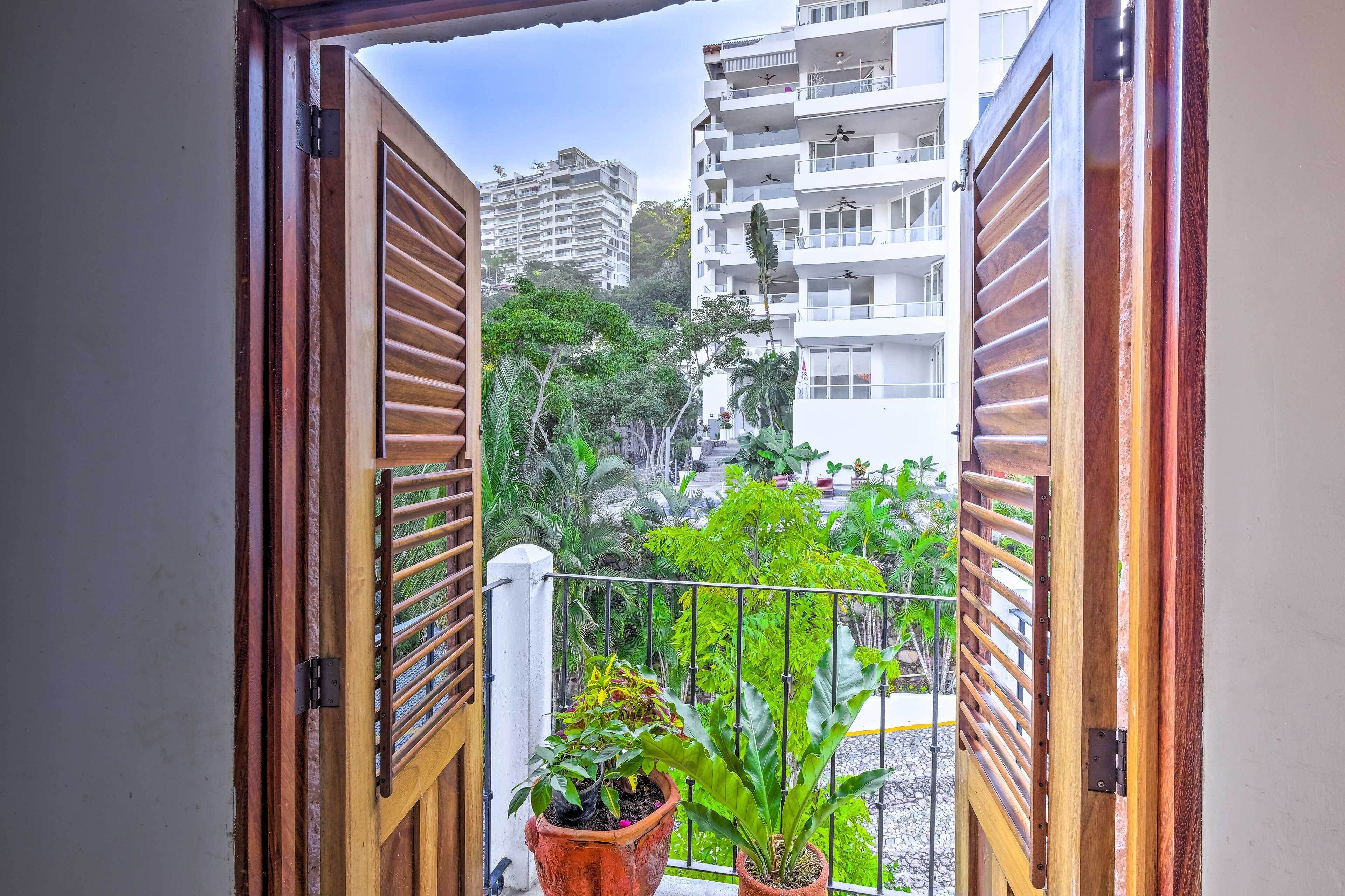 Eine offene Holztür mit Blick auf einen Balkon, Blumentöpfe und ein Gebäude im Hintergrund.