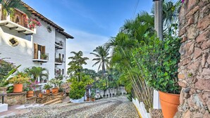 A cobblestone street lined with white buildings, potted plants, and palm trees. - Mid-century Modern Condo w/ Patio & Ocean Views! (Puerto Vallarta)