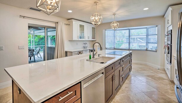 A modern kitchen with a large island, white cabinets, stainless steel appliances, and pendant lighting. - Pool Access & Beach Gear! Canalfront Naples Home (Naples)