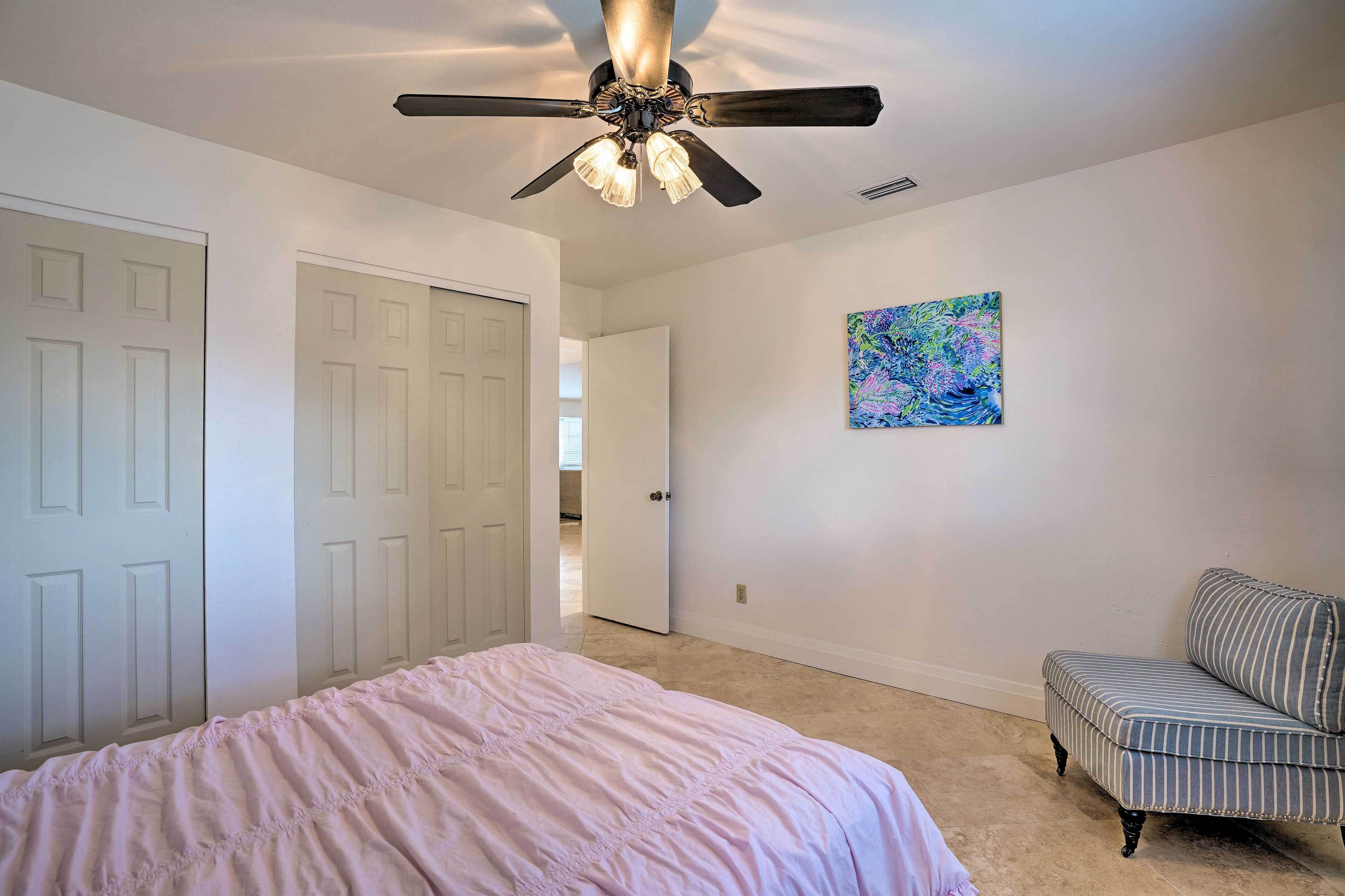 Un dormitorio con cama, ventilador de techo, una silla y una puerta.
