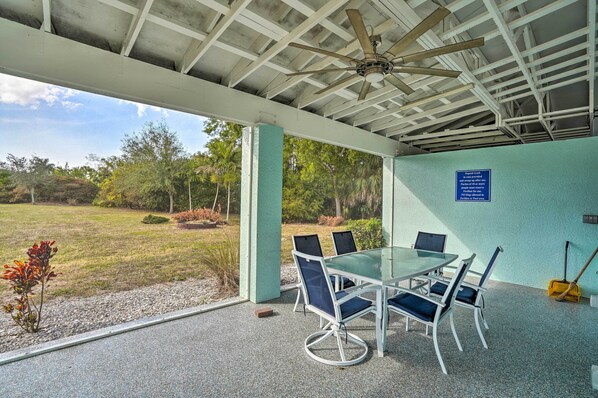 A covered outdoor area with a table and chairs, a ceiling fan, and a view of the surrounding landscape. - Pool Access & Beach Gear! Canalfront Naples Home (Naples)