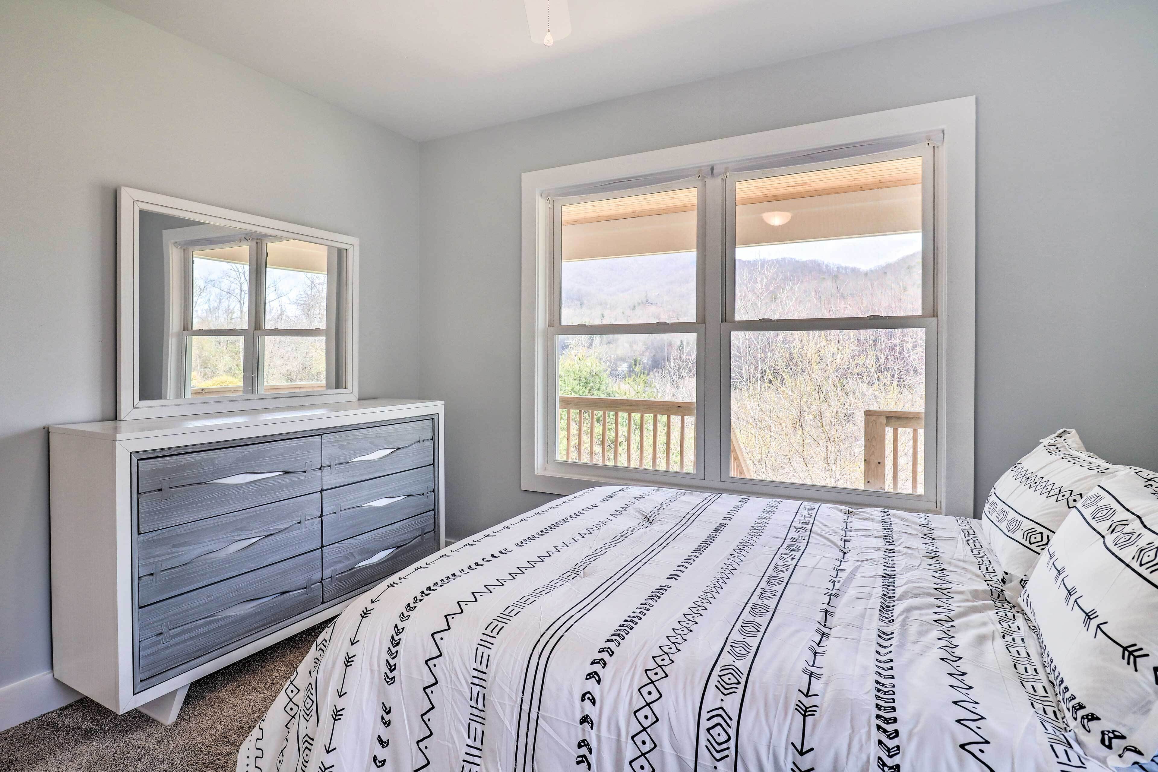 A bedroom with a bed, dresser, and a large window with a view.