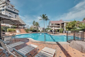 A swimming pool with lounge chairs, a thatched-roof structure, and palm trees. - Puerto Vallarta Condo w/ Bay Views + Pool Access! (Puerto Vallarta)