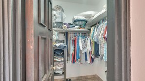A narrow hallway with a wooden door, a shoe rack with various shoes, and a clothing rack with multiple garments.