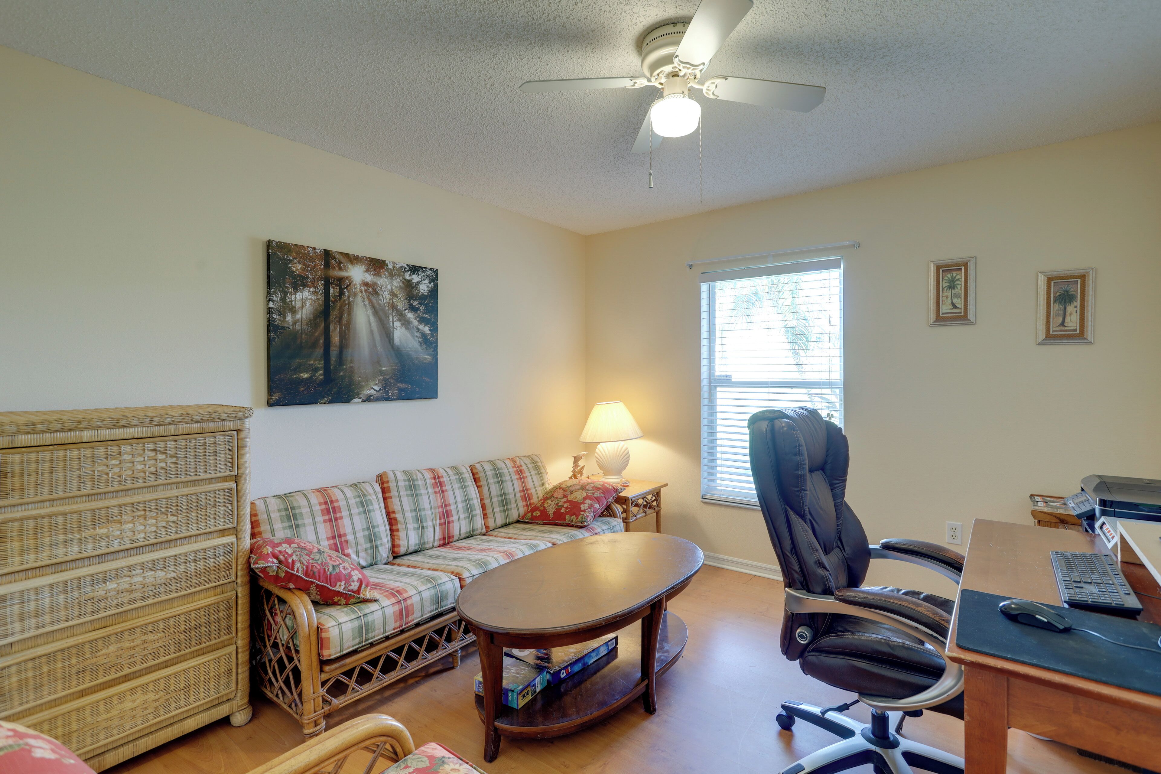 A living room with a sofa, a coffee table, a chair, a desk with a computer, and a ceiling fan.