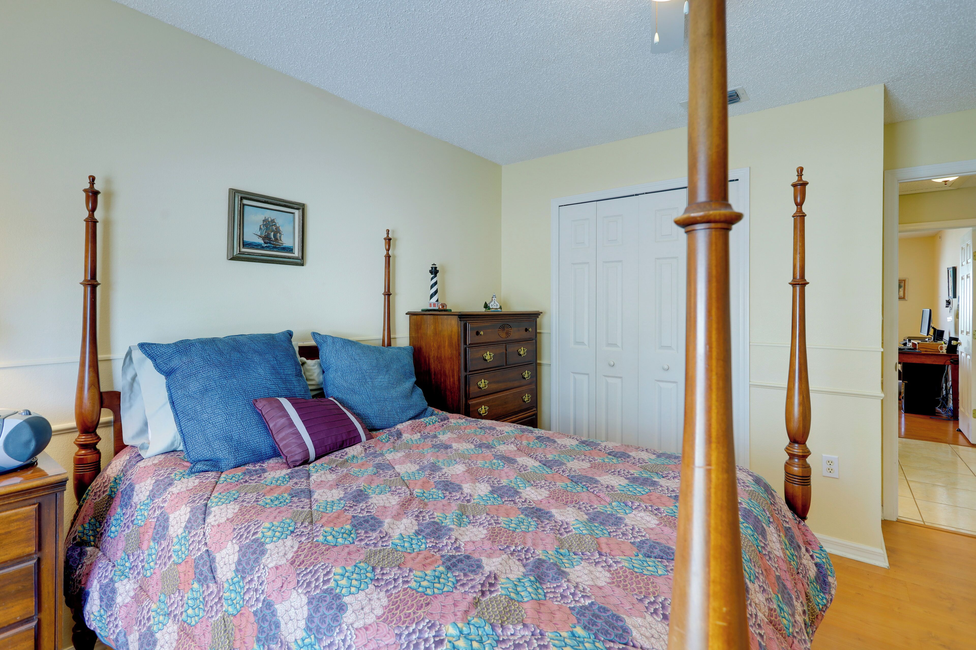 A bedroom with a four-poster bed, a dresser, a nightstand, and a door leading to another room.